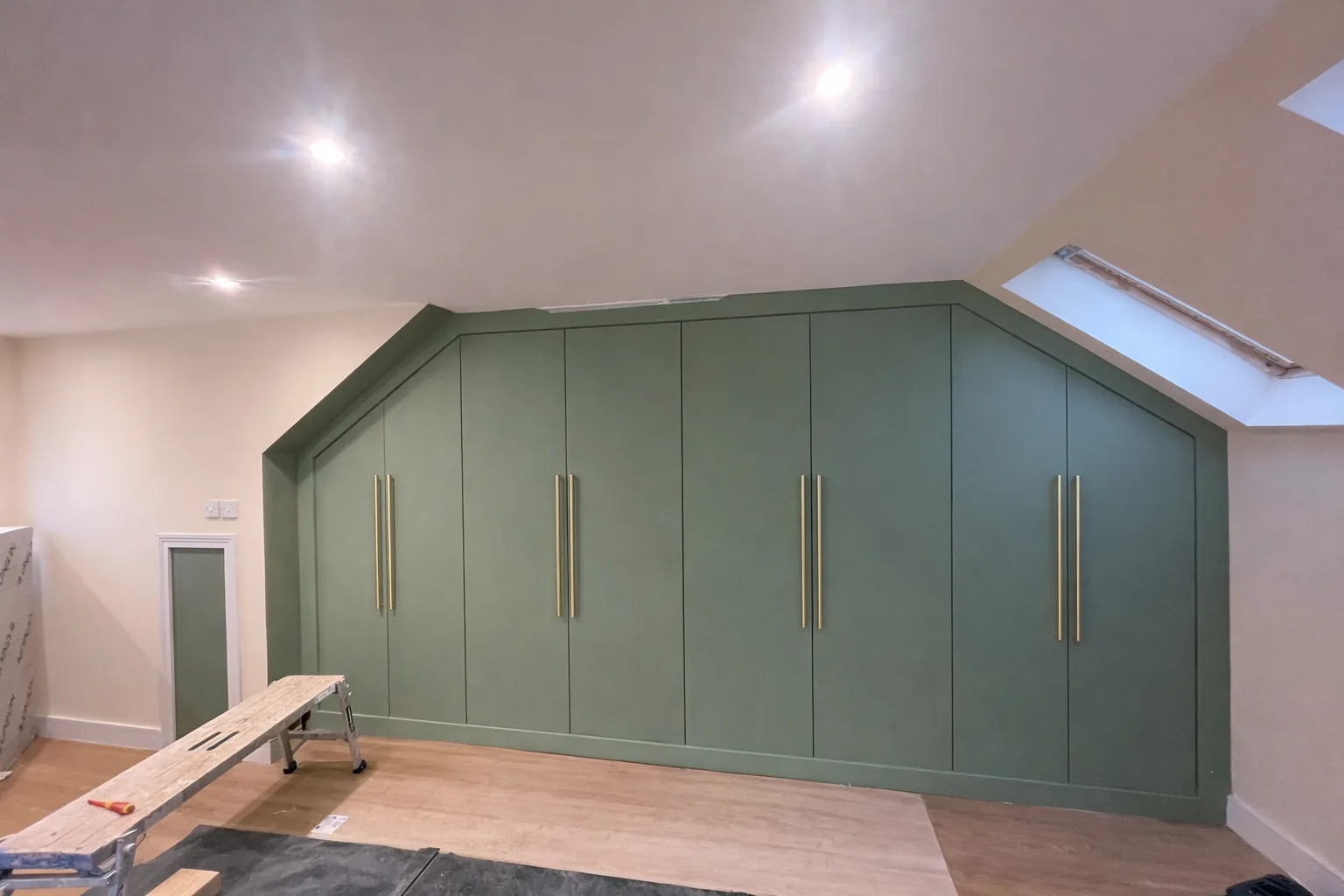 Green fitted wardrobes built beneath a sloping loft ceiling