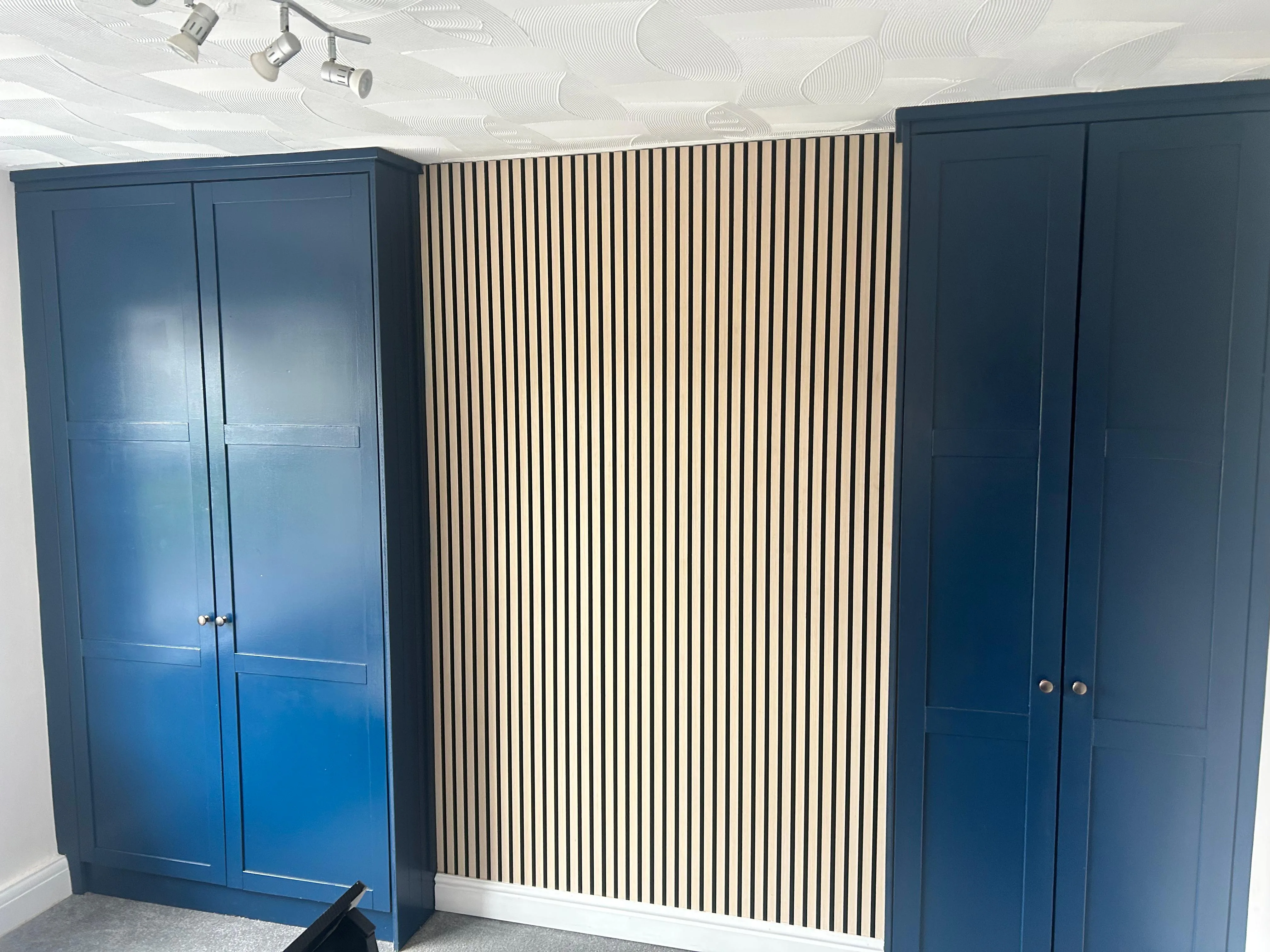 Blue shaker fitted cupboards either side of an oak slat feature panel