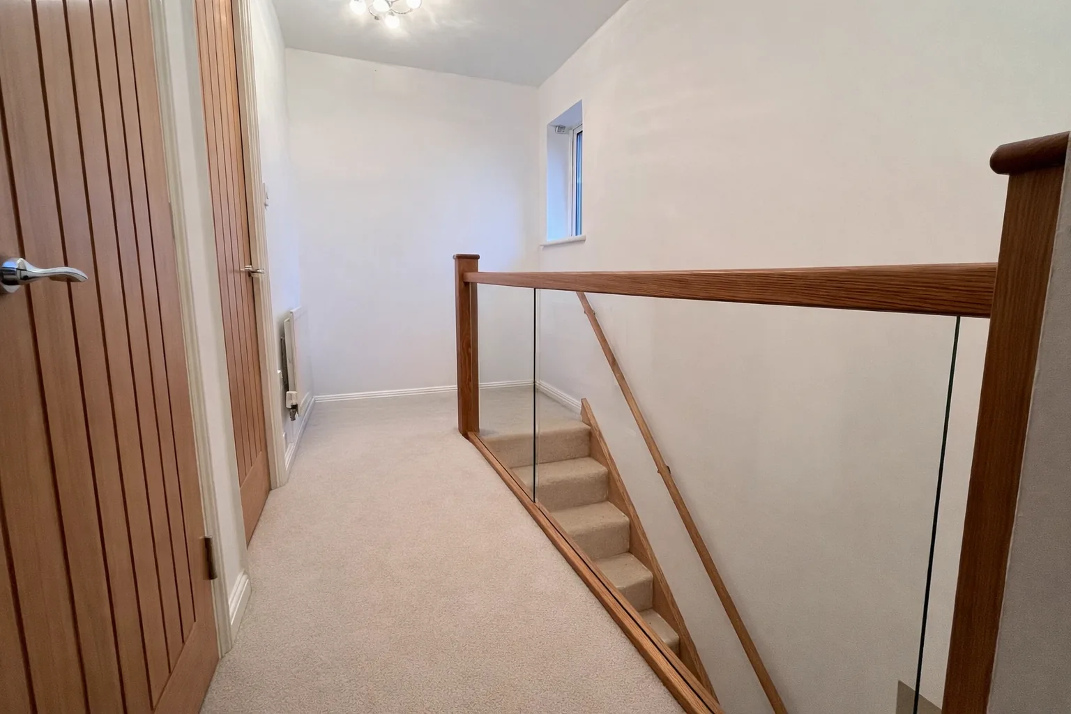 Glass balustrade with oak handrail beside oak internal doors in Neath Port Talbot